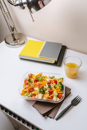Healthy food in lunch box, on working table with laptop .Ensalada de pasta brocoli con queso y verduras. eating at workplace. Home food for office conceptの写真素材