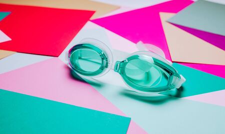 turquoise swimming glasses, with rubber strap on multicolor geometric background.の写真素材