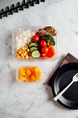 Healthy food in lunch box, on working table. Basmati rice with chickpeas, broccoli, tomato and carrot, bread and fruit for dessert. eating at workplace. Homemade food concept in the office or study placeの写真素材