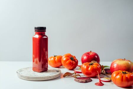 Red smoothie drink in bottle near ripe apples tomatoes and beets. Detox diet for healthy body and mind. health food concept. Front view on grey background の写真素材