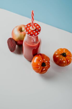 Red smoothie drink in bottle with straw surrounded by red apples, tomatoes and beets near ripe apples tomatoes and beets. Detox diet for healthy body and mind. health food concept.の写真素材