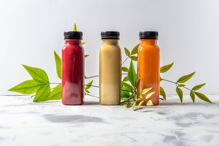 Red, orange and yellow smoothies and juices beverages in bottles with various fresh organic fruits and berries ingredients on white backgroundの写真素材