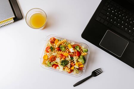 Healthy food in lunch box, on working table with laptop .Ensalada de pasta brocoli con queso y verduras. eating at workplace. Home food for office concept の写真素材