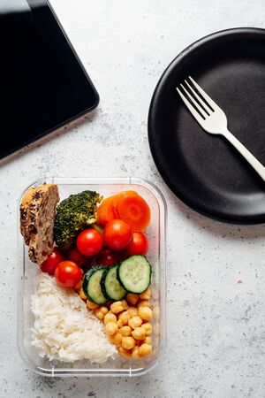 Healthy food in lunch box, on working table with the tablet. Basmati rice with chickpeas, broccoli, tomato and carrot, bread and fruit for dessert. eating at workplace. Homemade food concept in the office or study place
の写真素材
