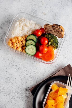 Healthy food in lunch box, on working table. Basmati rice with chickpeas, broccoli, tomato and carrot, bread and fruit for dessert. eating at workplace. Homemade food concept in the office or study placeの写真素材