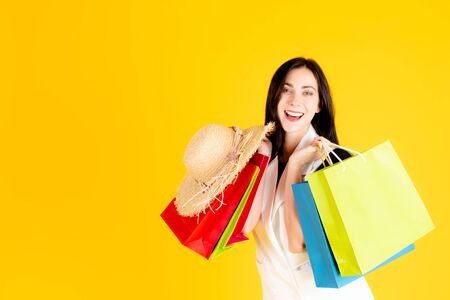 A young cute girl black-haired in a white dress is carrying colorful shopping bags and smiling with...