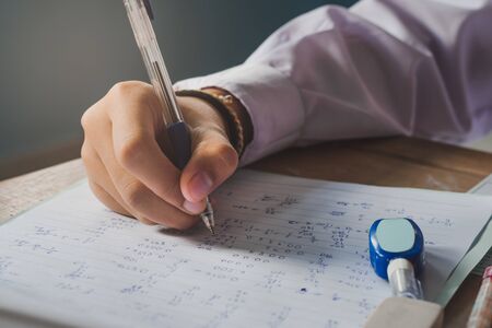 The hand of a girl student holding a pen to test the marks on the notebook during the examination. The hand is holding the pen to write the number to test for the correct answer. Hands and writing.の写真素材
