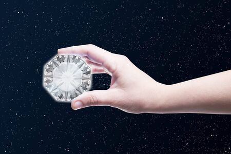Picture of a hand holding a big diamond with stars backrgound