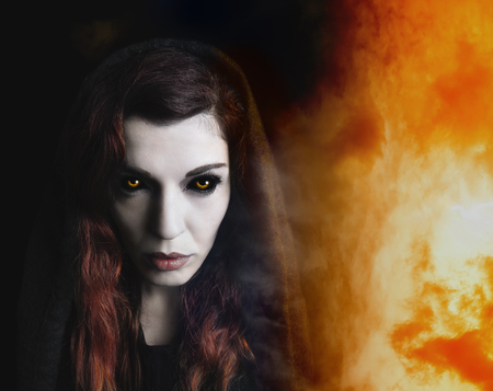 Intense portrait of a witch, fire in the background.の写真素材