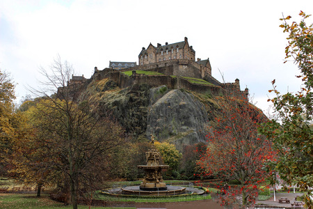 View of Edinburgh Castle and fountain on a cloudy day from Princes Street Garden in the early winter with autumn foliage.のeditorial素材