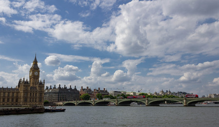 View of Big Ben and Westminster Bridge with iconic red buses crossing on a bright sunny day in London England.の写真素材