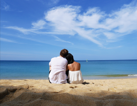A happy couple in white sitting together looking a beachの写真素材