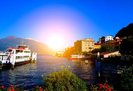Colorful village and boat in Bellagio along Lake Como in Italy with strong flare lightの写真素材
