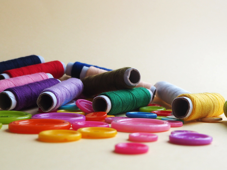 Sewing kit, colorful buttons in different sizes and multi-color thread on a light yellow background, hobby concept, selective focusの写真素材
