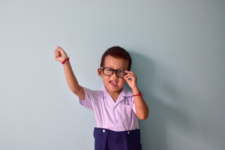 Back to school or first day to school concept, Little Asian kindergarten kid in glasses and school uniform with backpack being ready to go to school on light blue background with copy space for textの写真素材