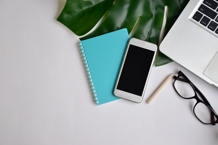 Blogger or modern office work space with laptop, light blue notebook, pencil, green mug of coffee, glasses, mobile phone on white table background with copy space for textの写真素材
