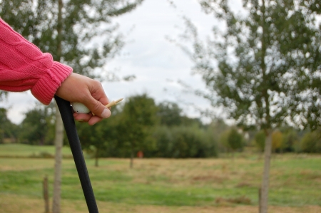 Golfer at rest, leaning on his club and holding a golf ball and tee in his handの写真素材