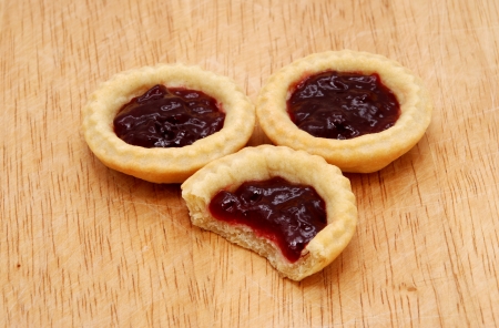 Three yummy jam tarts, one with a bite taken from it, on a wooden tableの写真素材