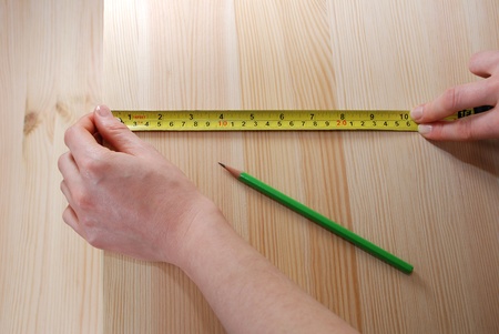 Two hands measuring a wooden board with a steel tape measure in inches and centimetres