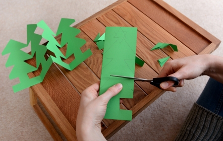 Woman cutting out a paper Christmas tree chain with scissorsの写真素材