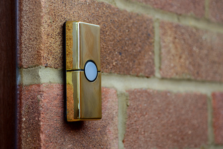 Gold or brass coloured doorbell on the brick wall of a houseの写真素材