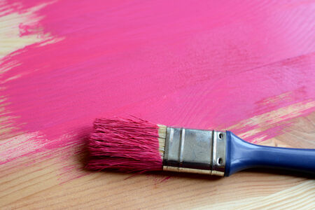 Paint-covered paintbrush on half-painted wooden boardの写真素材