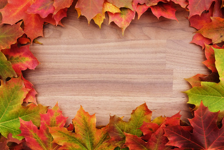 Fall-themed border of autumnal maple leaves around a walnut wood background