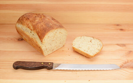 Bread knife with freshly sliced loaf of oat and linseed bread on a wooden table