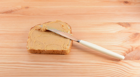 Slice of fresh bread being spread with smooth peanut butter, on a wooden tableの写真素材