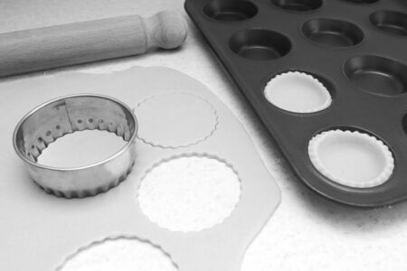 Lining a bun tin with circles of rolled out pastry to make mince pies, with a rolling pin on the...