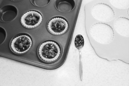 Making mince pies in the kitchen - filled pastry cases, mincemeat, dough scraps and teaspoon - monochrome processingの写真素材