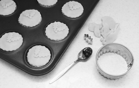 Uncooked mince pies in a bun tin, pastry leftovers, teaspoon and cutters - monochrome processingの写真素材