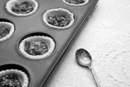 Filled, uncooked jam tarts in a tin, with a jam-covered teaspoon beside - monochrome processingの写真素材