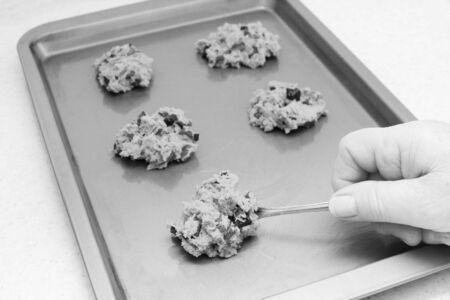 Spooning chocolate chip and pecan cookie dough onto a baking sheet - monochrome processingの写真素材