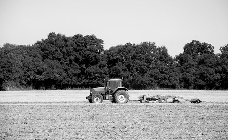 Tractor and disc harrow breaking up the soil after harvest in a farm field - Kent, England -...