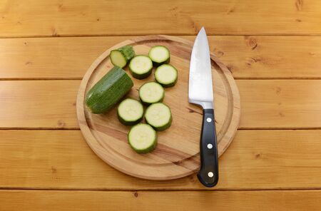 Fresh green courgette being sliced with a sharp kitchen knife on a wooden chopping boardの写真素材