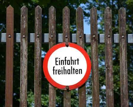 Round German sign on a wooden fence instructs Keep entrance clear - Einfahrt freihalten