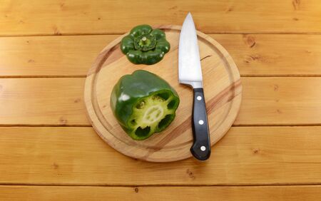 Raw green pepper sliced open with a sharp kitchen knife on a wooden chopping board, focus on the seeds and membrane insideの写真素材
