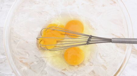 Beating three eggs with a wire balloon whisk, one yolk broken, in a glass bowlの写真素材