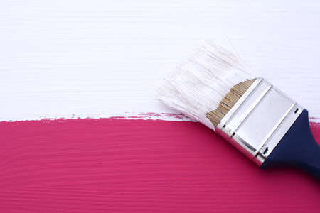 Painting pink wooden surface with white paint, dirty paintbrush lies on topの写真素材