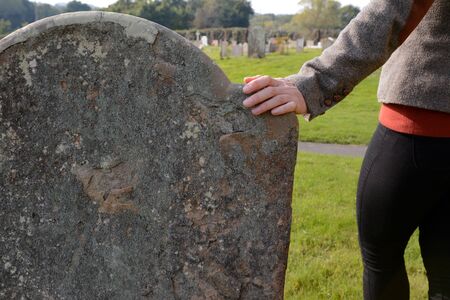 Woman's hand resting on an anonymous headstone in a rural graveyardの写真素材
