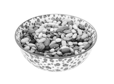 Mixed dried beans - black turtle beans, flageolet beans, pinto beans, brown beans, haricot beans and split peas -  in a porcelain bowl with a floral design, isolated on a white background - monochrome processingの写真素材