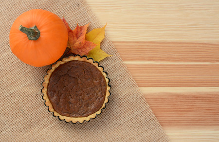 Sugar pumpkin and mini pumpkin pie with autumn maple leaves on hessian and wood, with copy spaceの写真素材