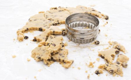 Circular cookie cutter with scraps of chocolate chip biscuit dough on a kitchen work surface