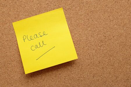 Yellow sticky note with Please Call written on it, stuck to an empty cork notice board with copy spaceの写真素材