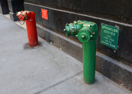 Red and green siamese standpipes on a sidewalk with theatre-related information signsの写真素材
