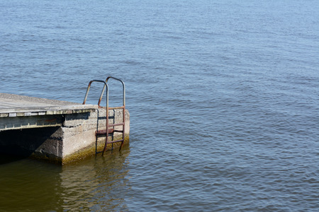 Rusted metal ladder on the side of a jetty, reaching down into water - with copy spaceの写真素材