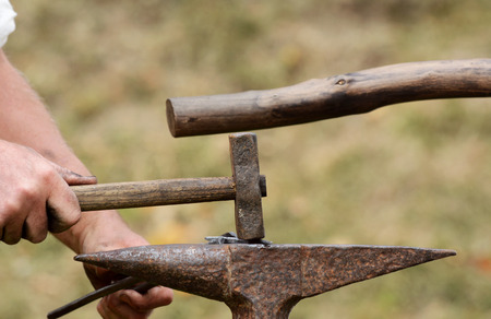 Close-up of man's hand using a rustic hammer to work a piece of metal on an anvil at a Medieval Fairの写真素材