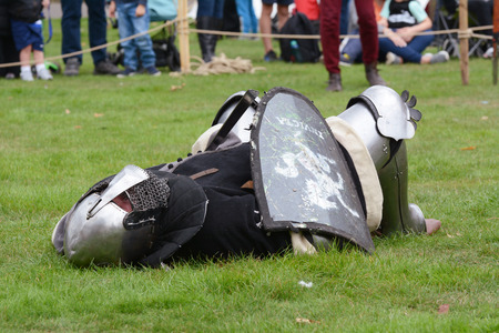 TONBRIDGE, ENGLAND - SEPTEMBER 8, 2018: Middle Ages warrior in full armour, carrying a shield, lies on the ground in defeat at the Medieval Fair at Tonbridge Castleのeditorial素材