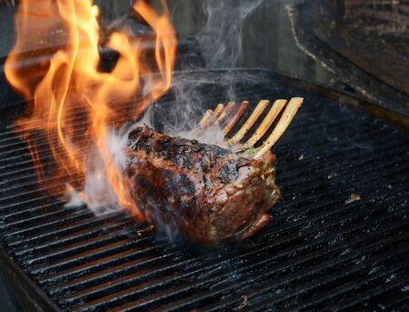 Rack of lamb on a barbecue. A flash of flame and cloud of smoke escapes from the grill around the...